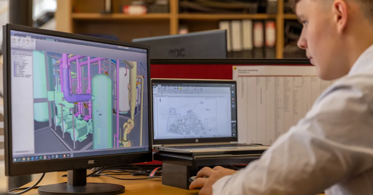 Engineer working with CAD software on two monitors at an office workstation, a 3D part model on screen