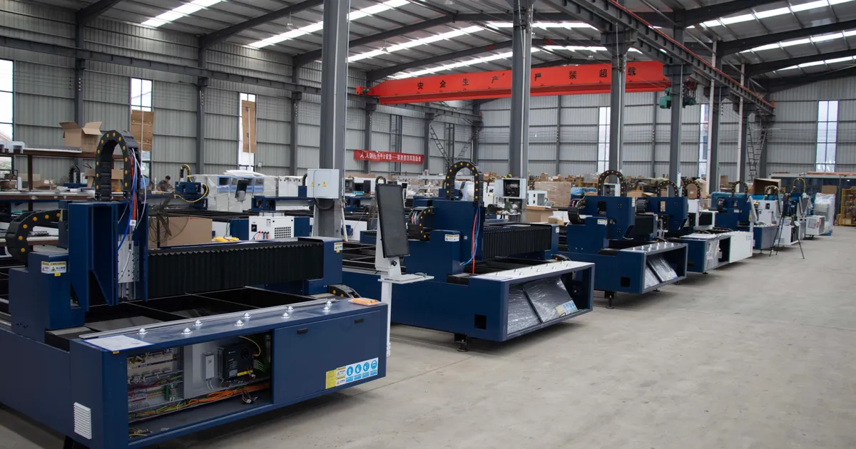 Row of large blue industrial machines lined up on the concrete floor of a factory hall with an overhead crane